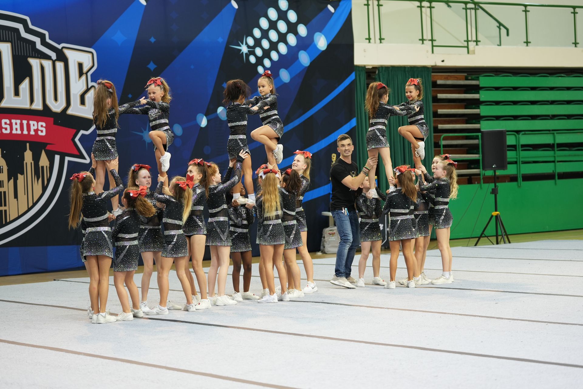 Cheerleading team performing a pyramid at a competition. Blue and black uniforms, indoors.