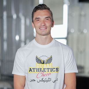 Man wearing white t-shirt with Dubai Athletics Cheer logo, smiling.