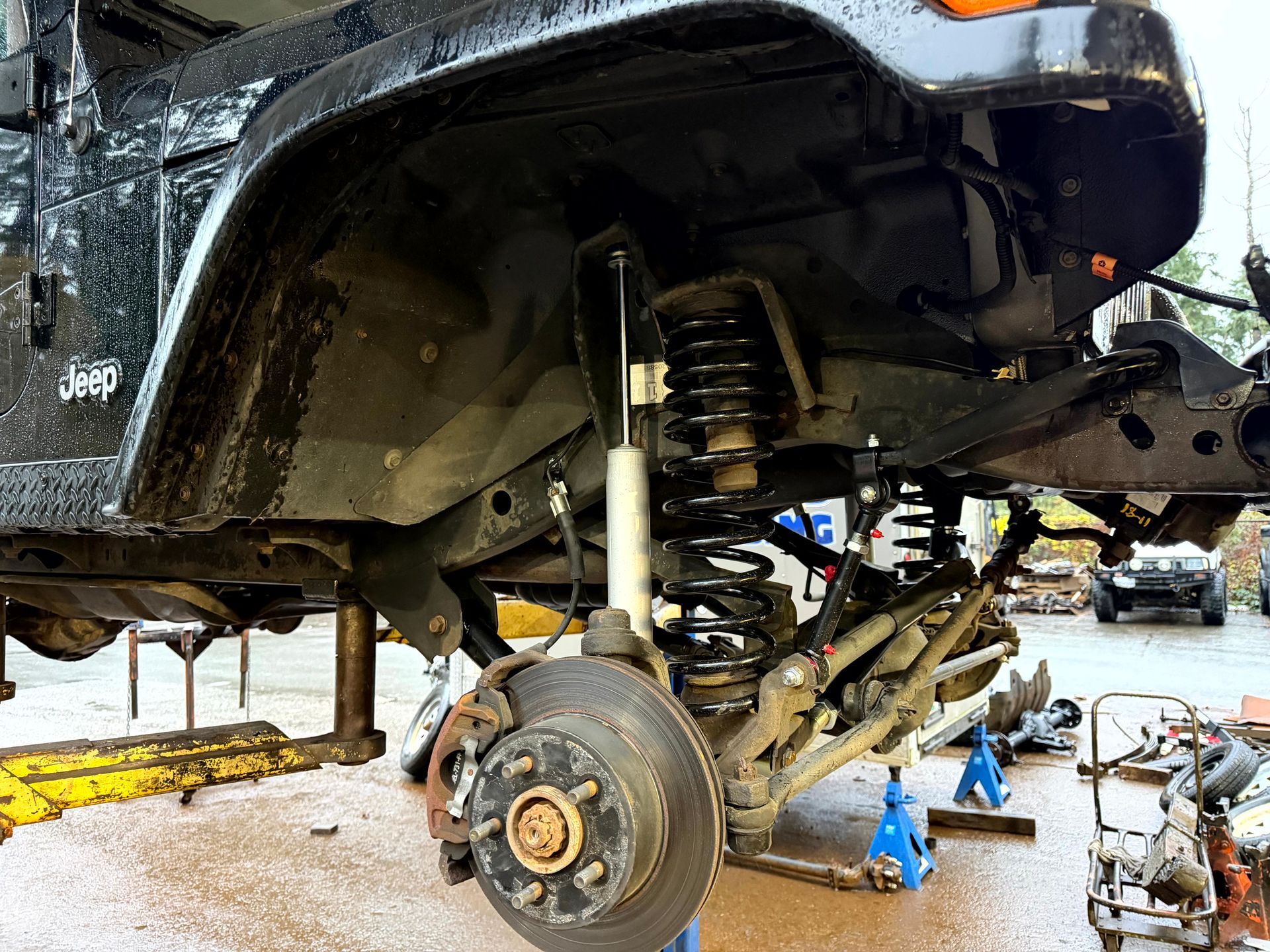 Black Jeep on jacks, front wheel and suspension removed, showing components during repair.