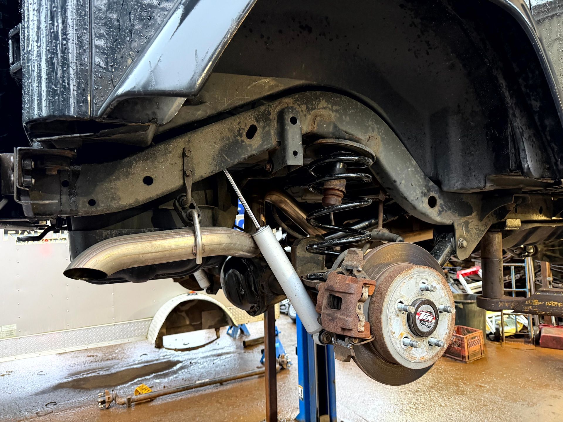 Rear suspension of a black off-road vehicle; tire removed, rust visible, shock absorber, exhaust pipe, and spring.