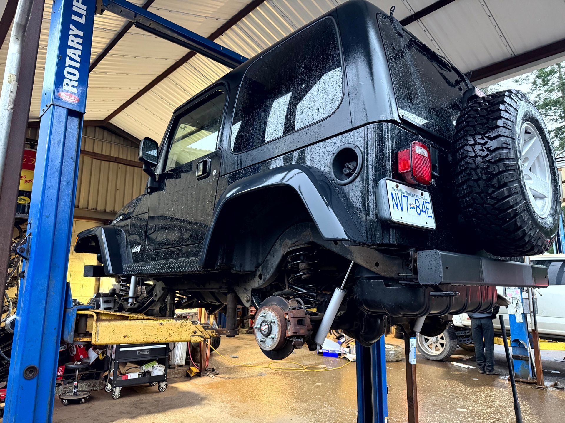 Black Jeep Wrangler on a hydraulic lift in a garage, undergoing repair.