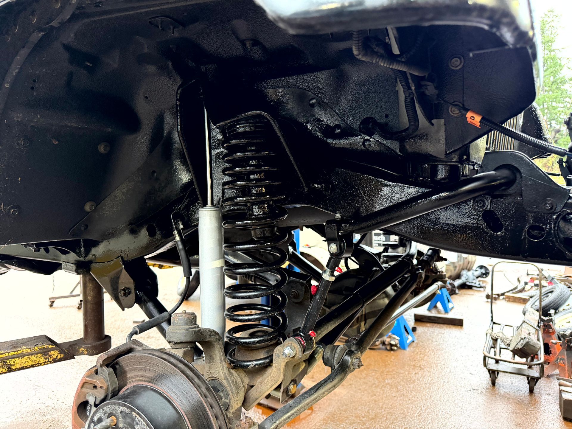 Black-painted vehicle suspension with coil spring and shock absorber, viewed from below.