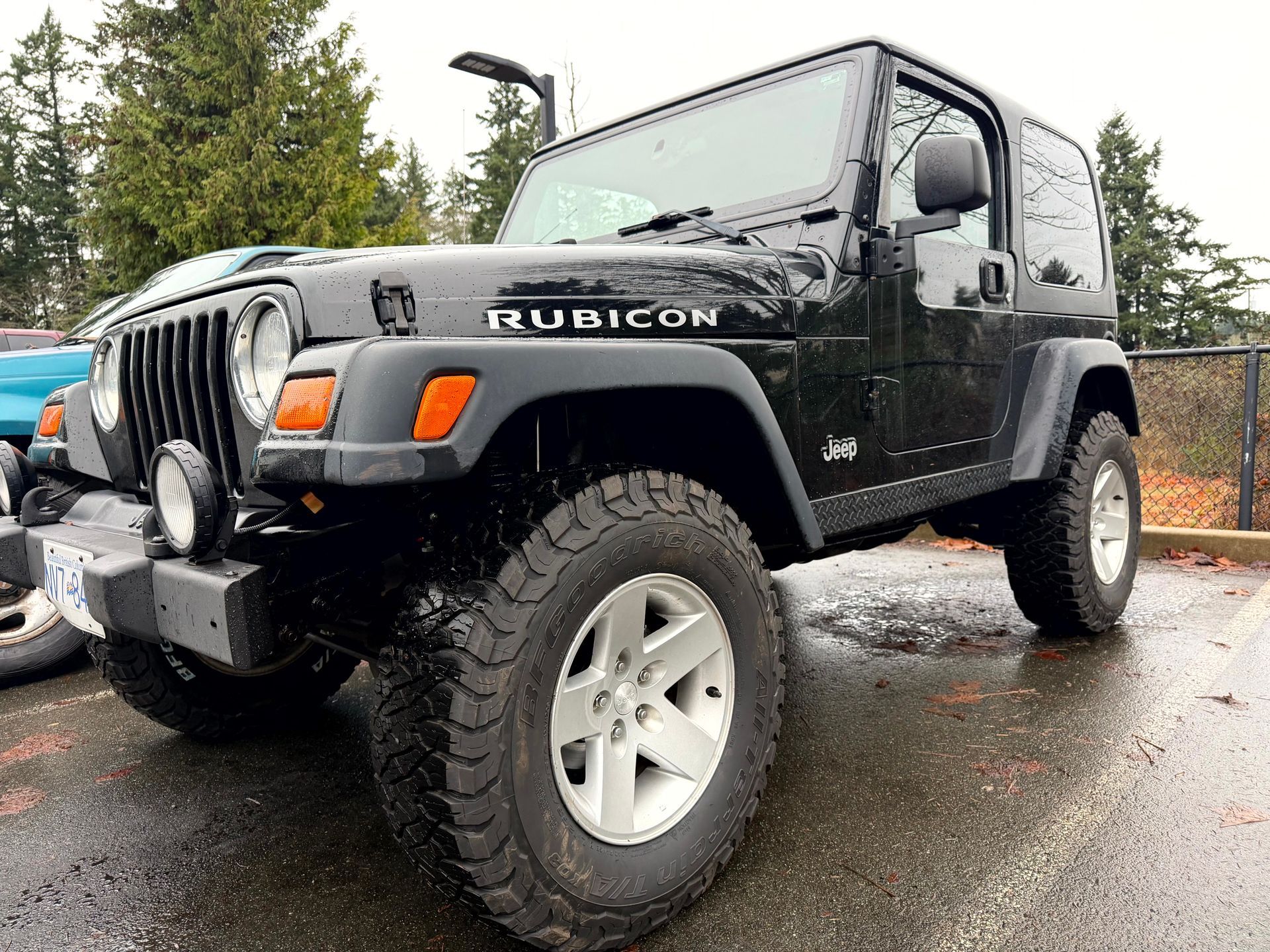 Black Jeep Rubicon with off-road tires parked on a wet surface.