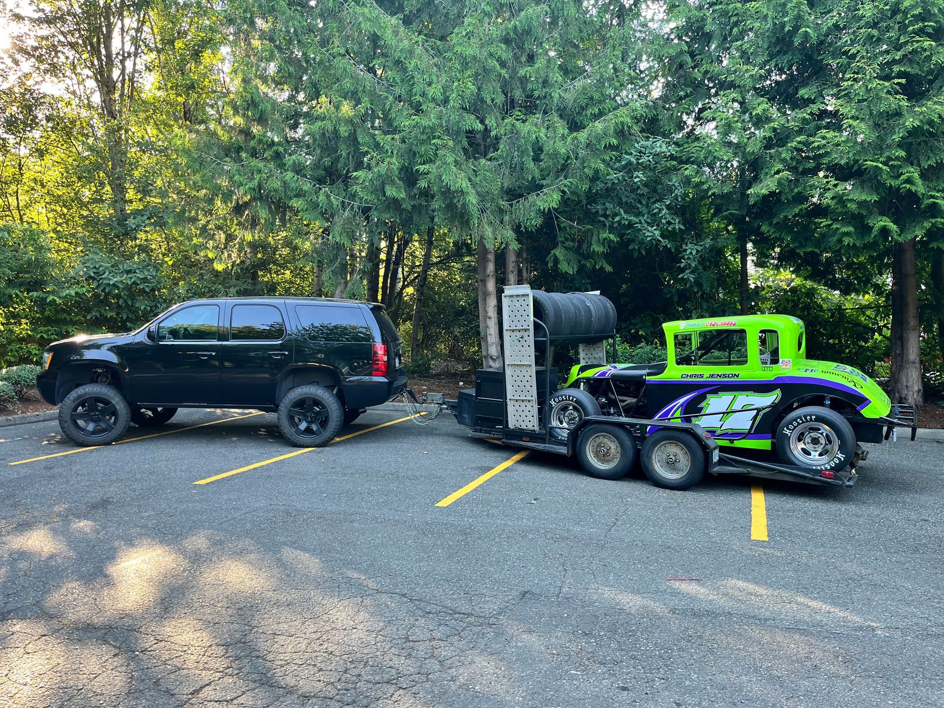 Black SUV towing a trailer with a green and black race car parked in a lot.