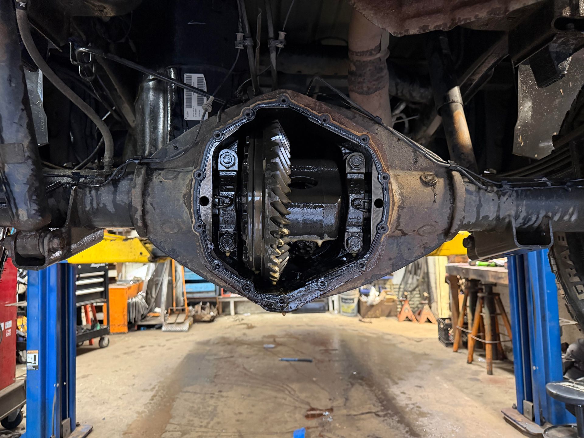Open rear differential of a vehicle, revealing gears and oil. Car is raised on a lift in a garage.