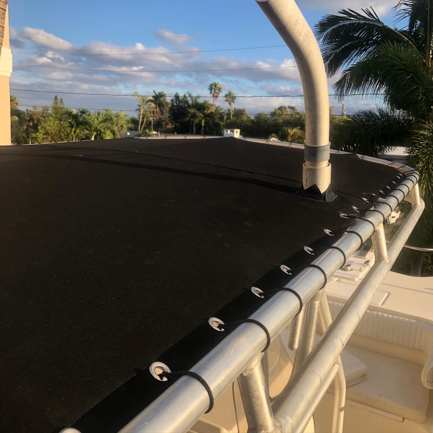 Boat's black sunshade with white railing, partially visible palm trees, and sky.