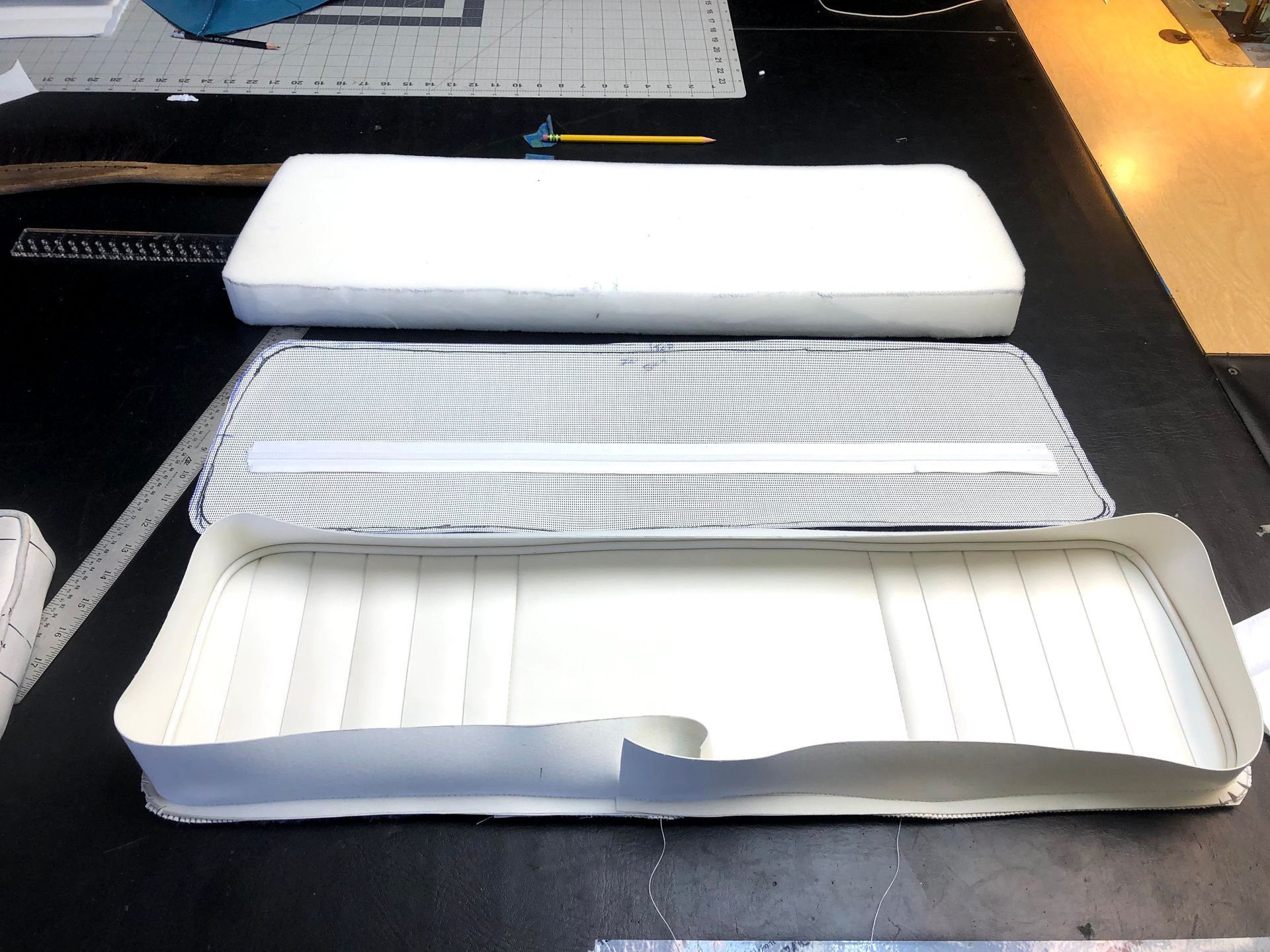 Three pieces of a white boat seat: foam cushion, mesh, and stitched vinyl base.