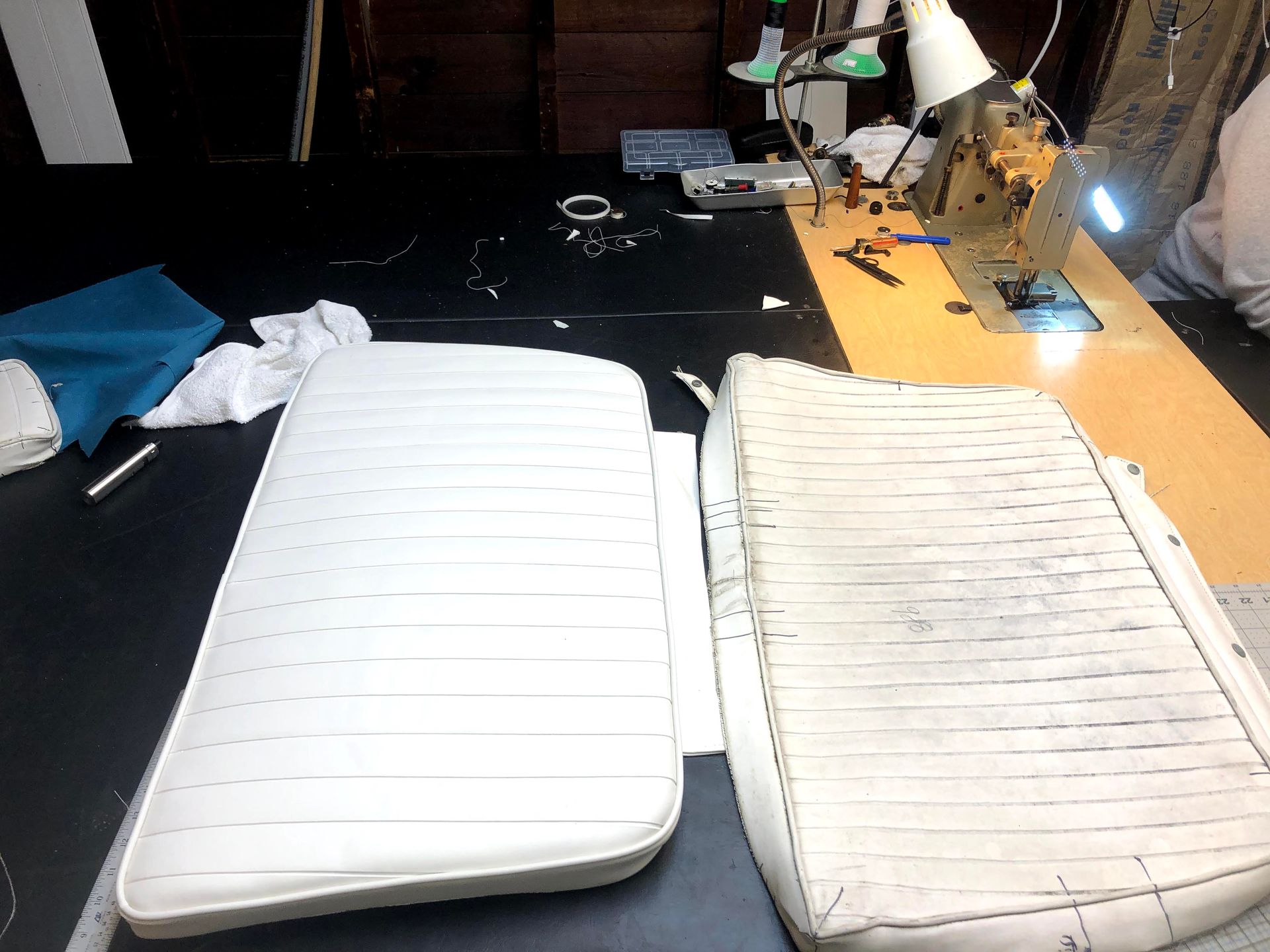 Two boat seat cushions: a new white one and an old, worn cream-colored one, on a workshop table.