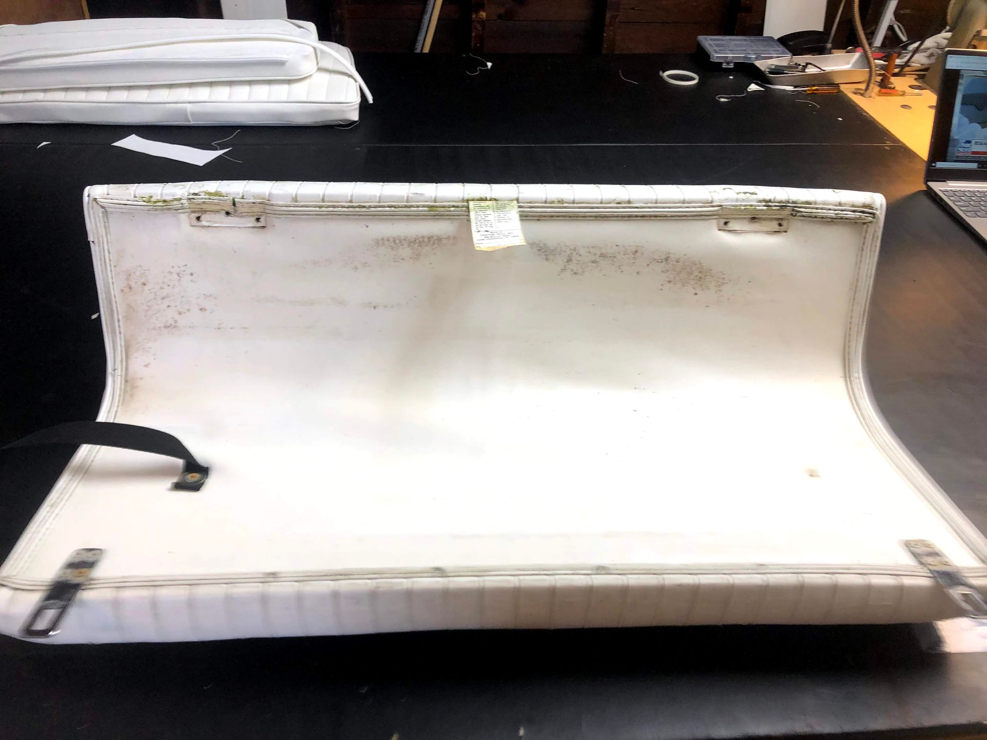 White boat seat, open, revealing interior. Brown discoloration, metal hinges and black strap visible.