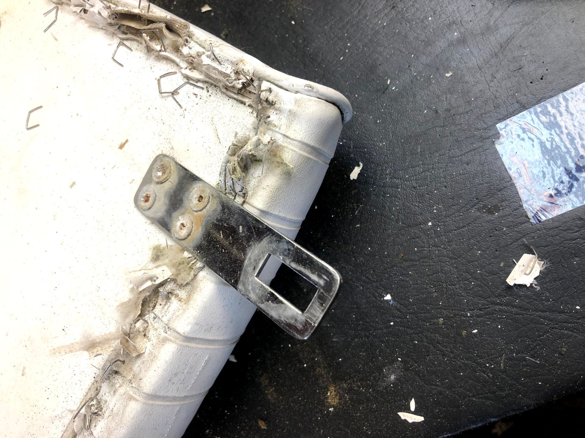 Metal seatbelt buckle on worn, white vinyl padding.