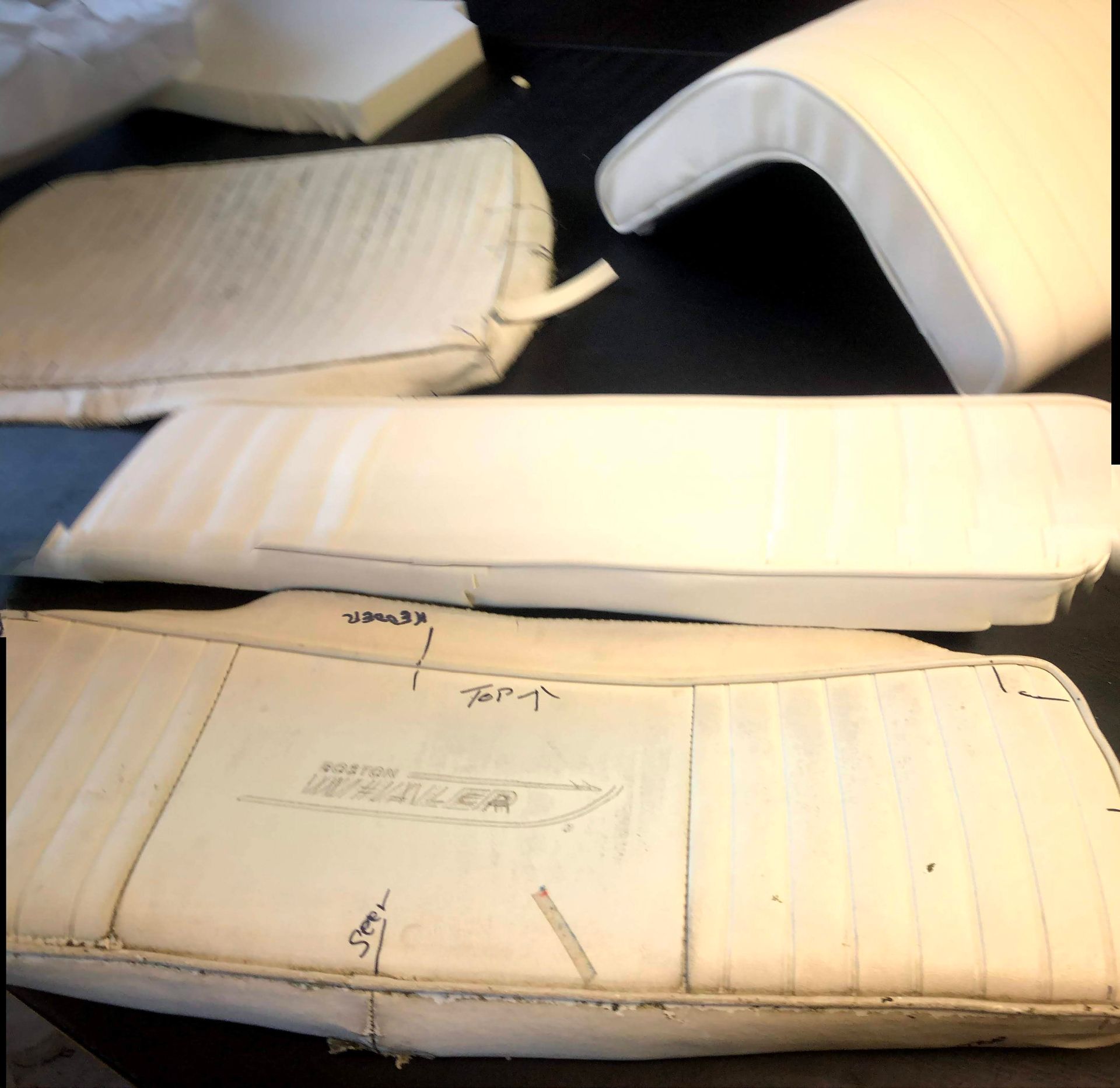Several cream-colored boat seat cushions, some finished and some with stitching lines, on a dark surface.