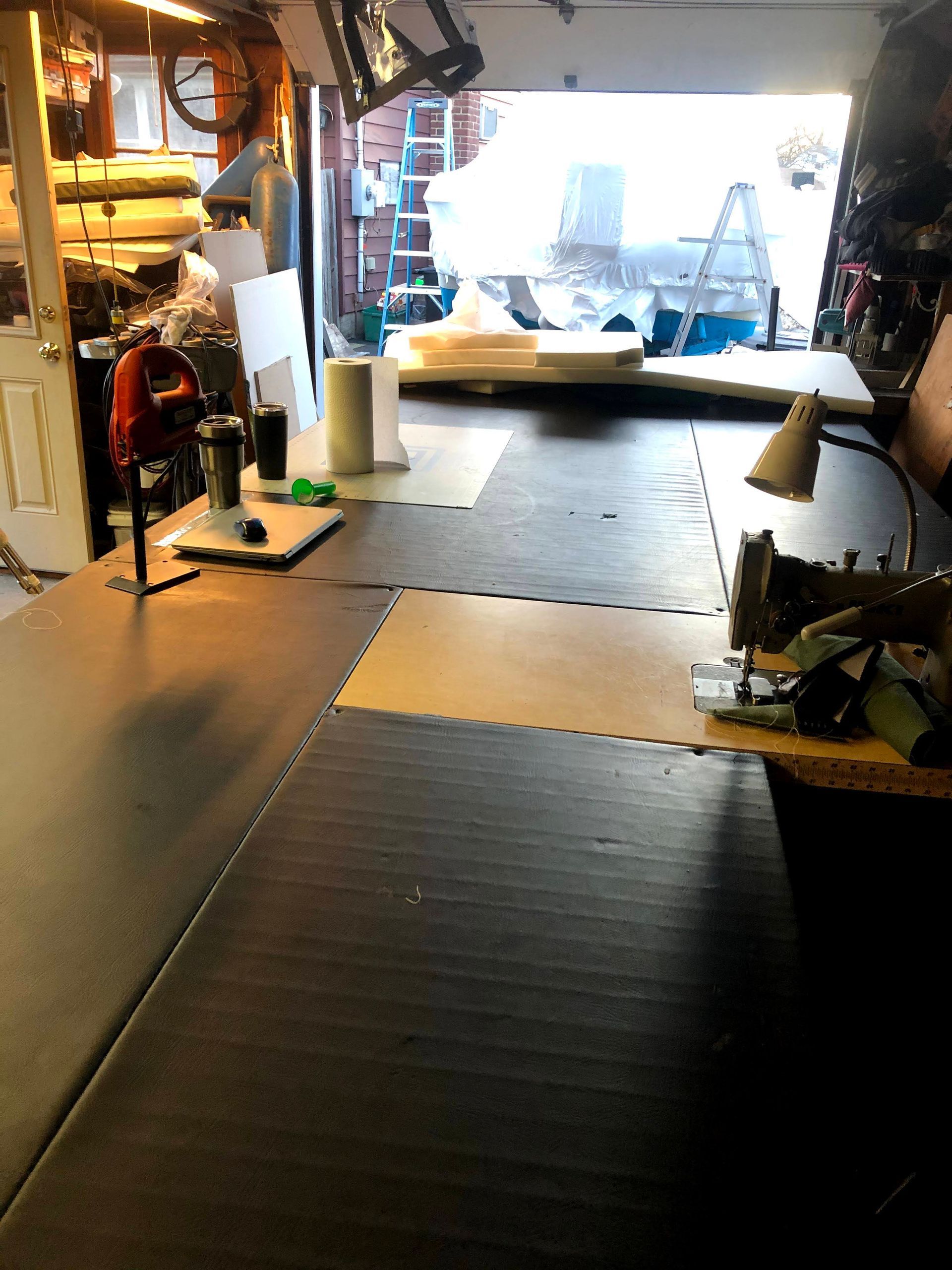 Workshop with a large dark table; sewing machine at right. Bright light through a large opening.