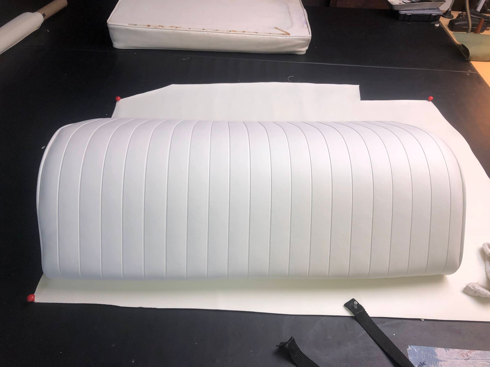 White upholstered cushion with vertical stitching on a black surface.