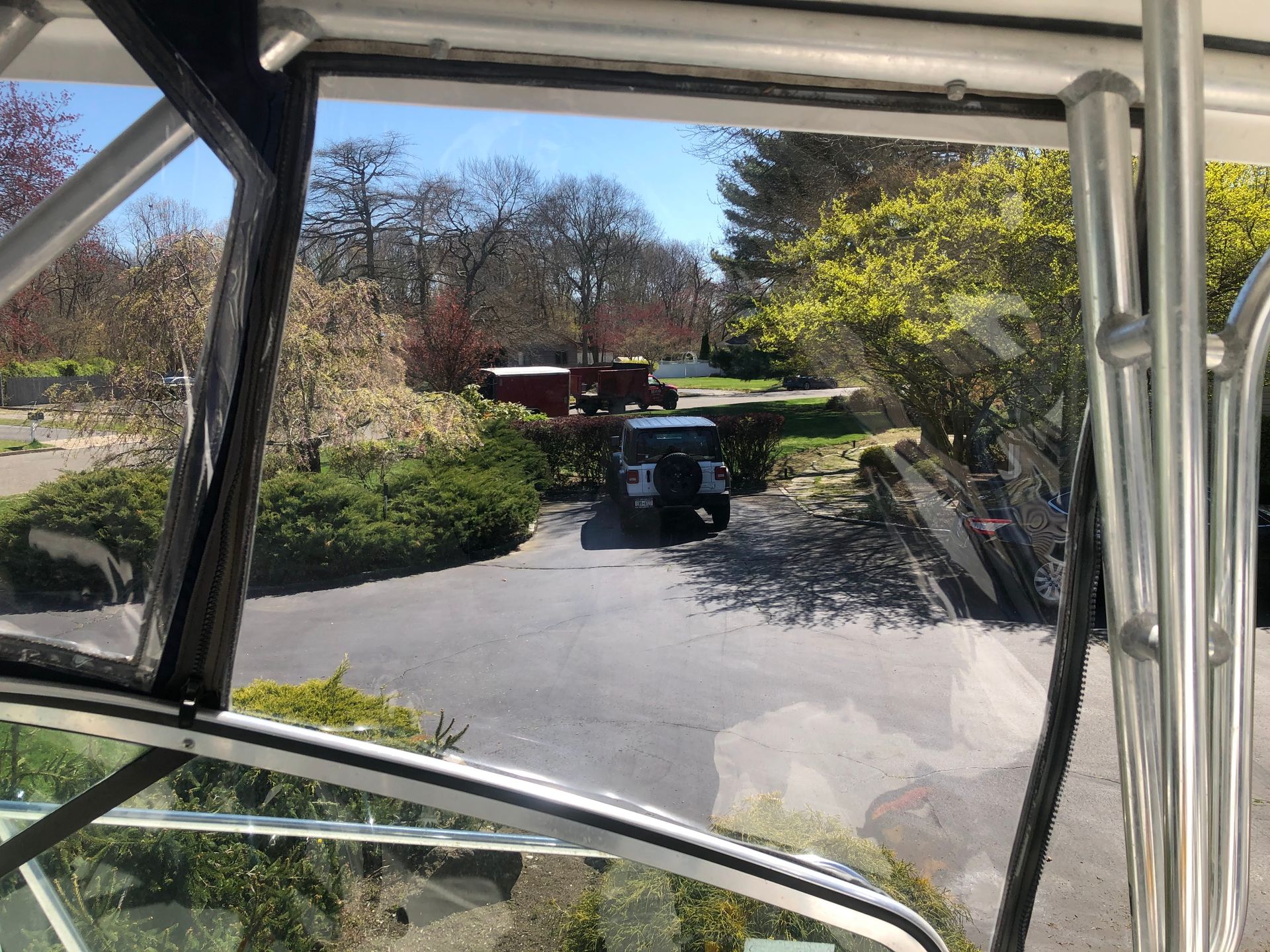 View from inside a vehicle through a window, showing a driveway with a truck and trees on a sunny day.