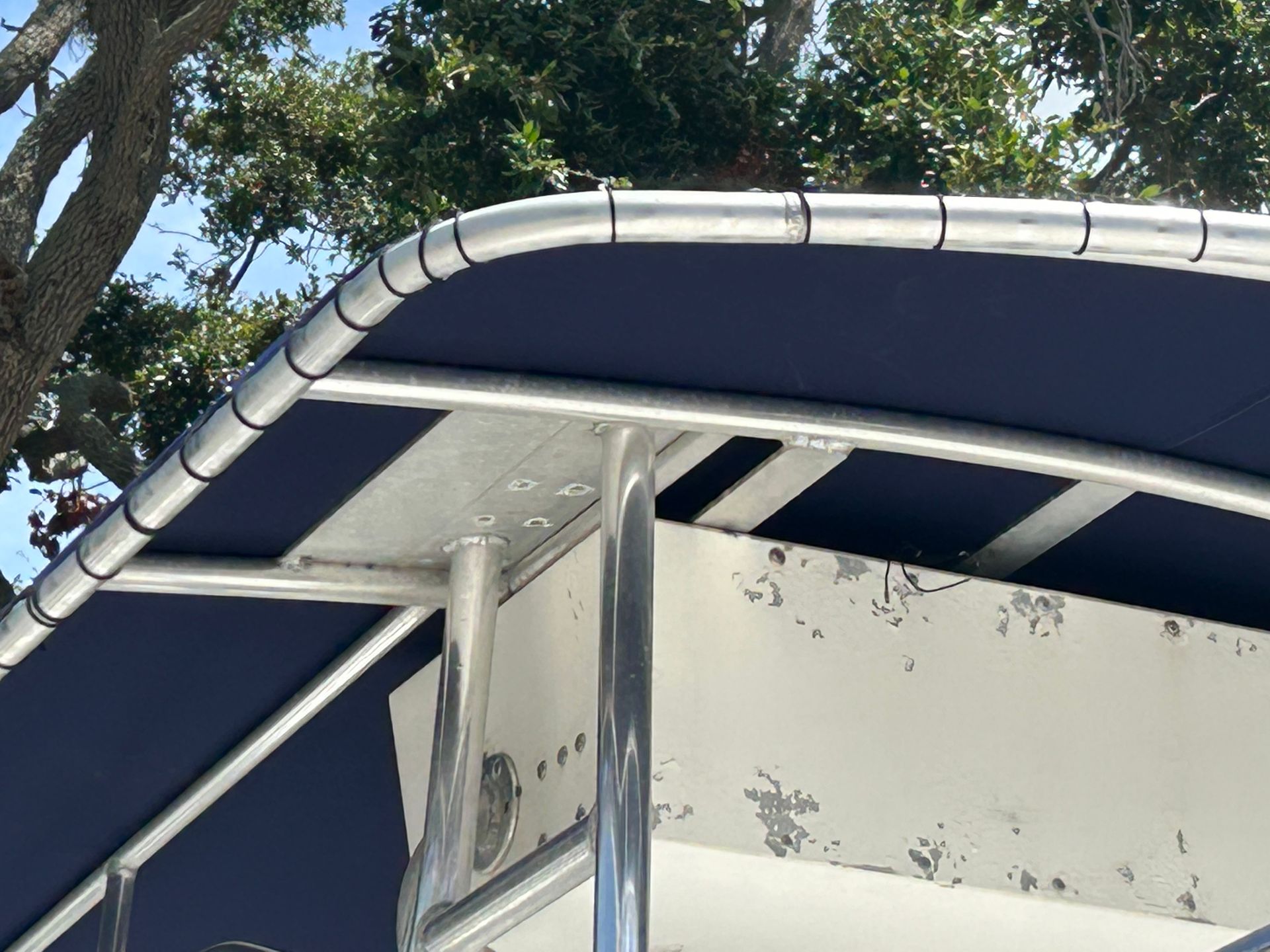 Close-up of a boat's aluminum frame and navy blue canvas top, set against trees and sky.