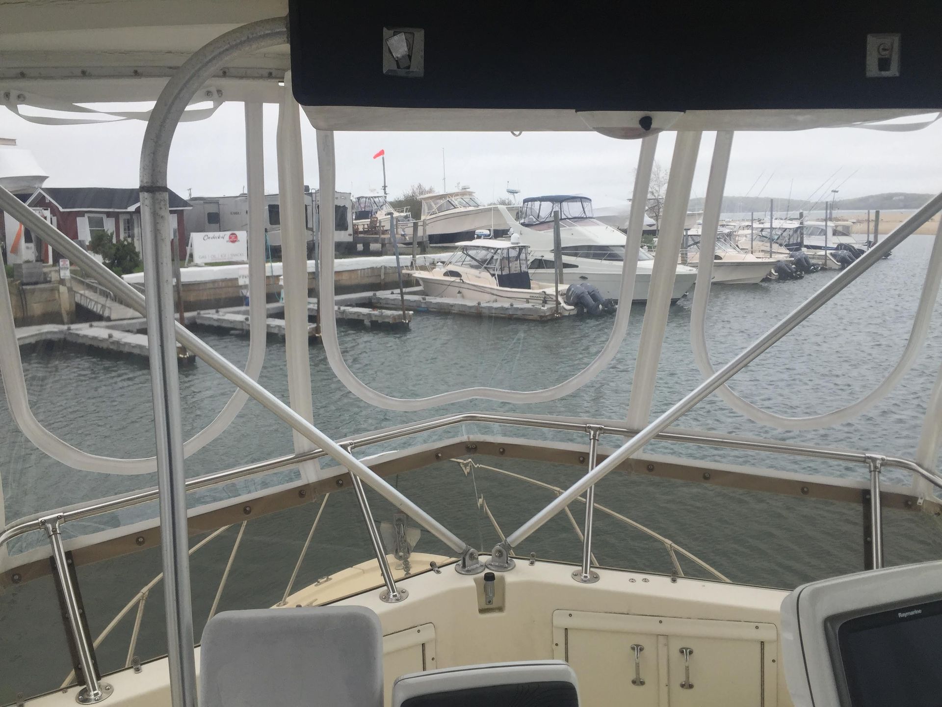 View from boat cockpit overlooking a harbor with docked boats, buildings, and overcast sky.