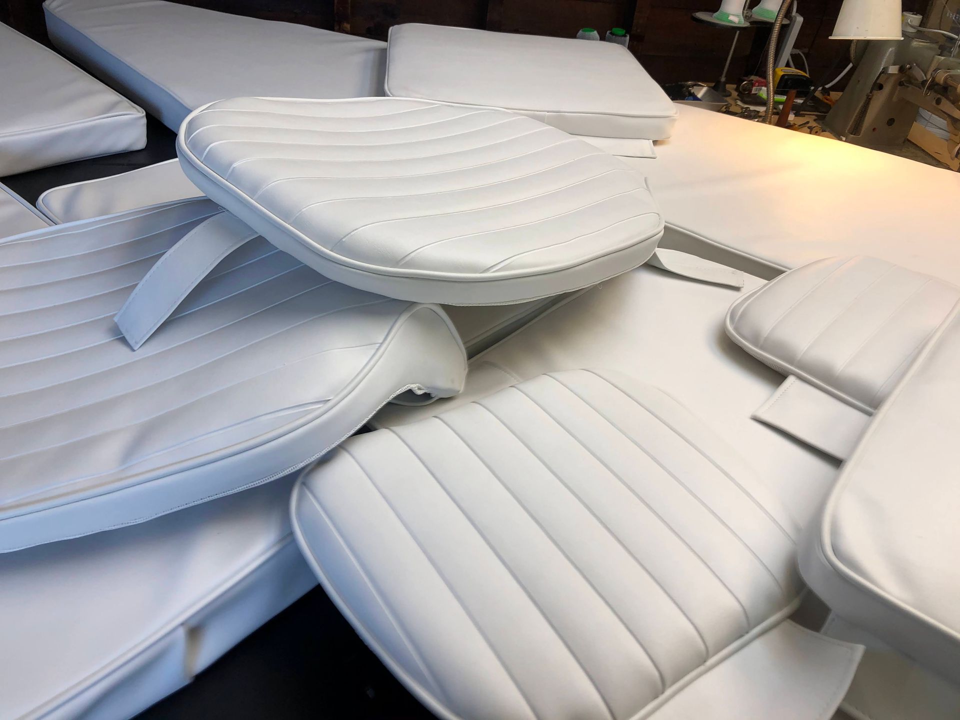 White upholstered boat cushions and seats, some with vertical stitched details, piled up on a table.