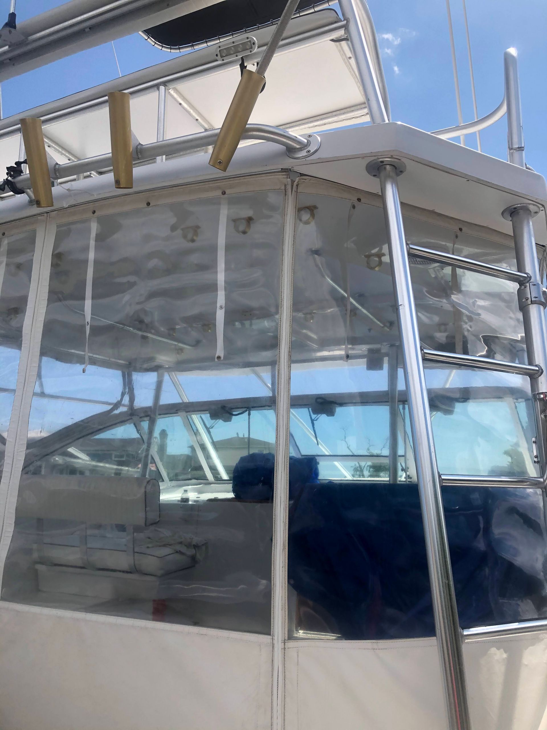 Boat cabin with clear vinyl enclosure. Stainless steel frame, blue tinted glass windows. Sunny outdoor setting.