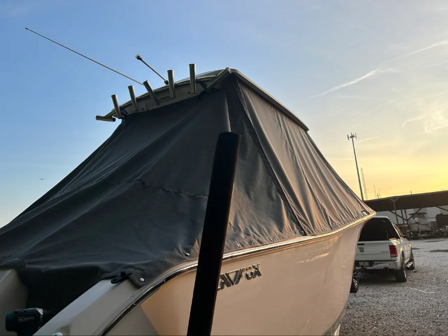 White boat with black cover, fishing rods, parked at dusk near a pickup truck.