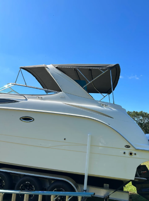 White boat with a gray canopy on a trailer against a blue sky.