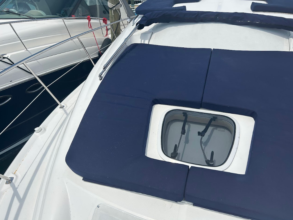 Blue cushions on a white boat deck, surrounding a window. Another boat is docked nearby.