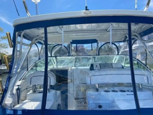 A boat's interior with clear vinyl enclosure, blue trim, white seats, and instrument panel.