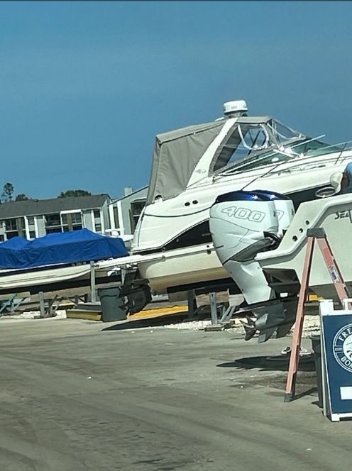 Boats on supports in a marina. One has a gray cover. Blue sky in background.