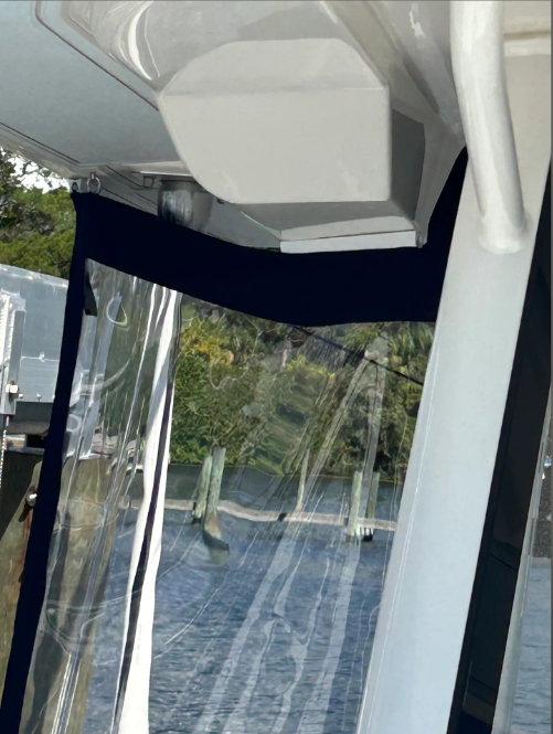 White boat structure with dark blue fabric, clear plastic curtains, and a view of the water.