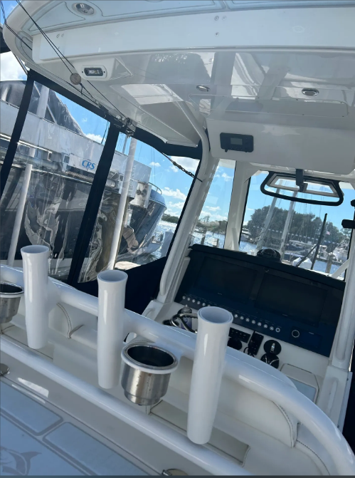 Interior view of a white boat's helm with windshield, rod holders, and a blue-sky background.