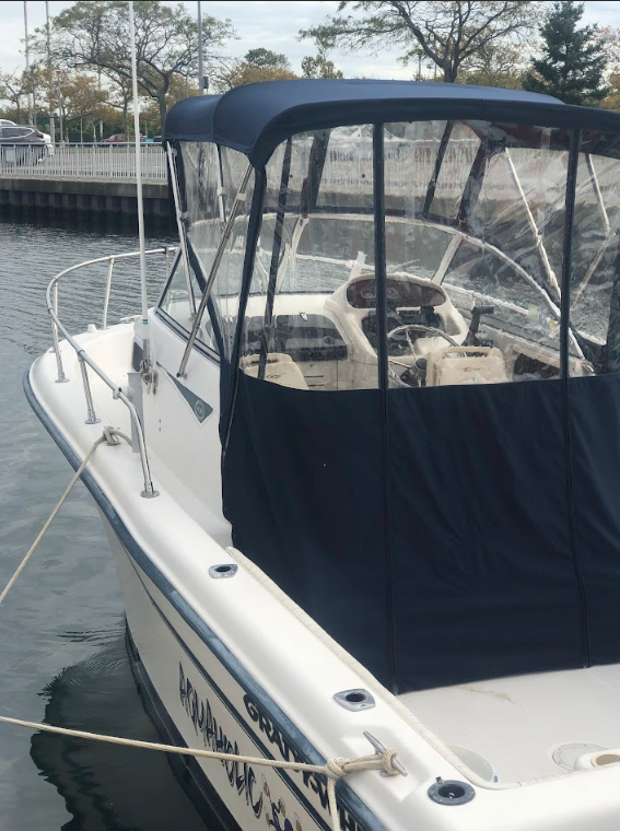 White boat with a dark blue canopy and clear vinyl windows, docked near a harbor.