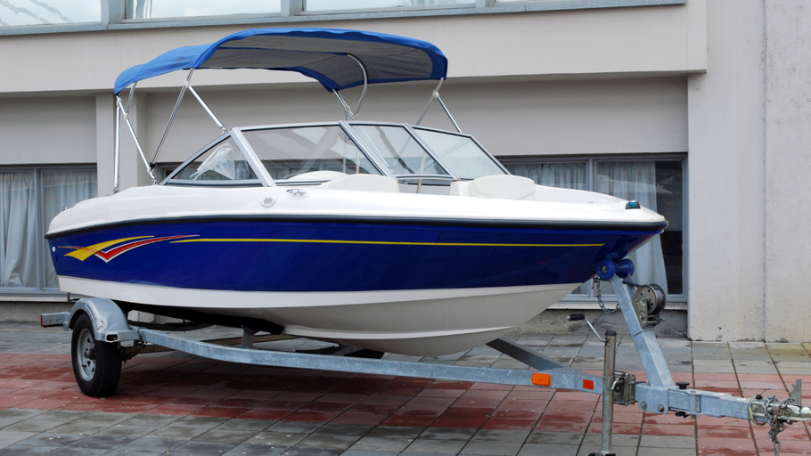 Blue and white motorboat on a trailer, parked outside. Features a blue sunshade.