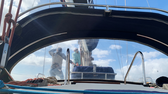 View from sailboat cockpit, two people near mast in blue and white, working on a boat.