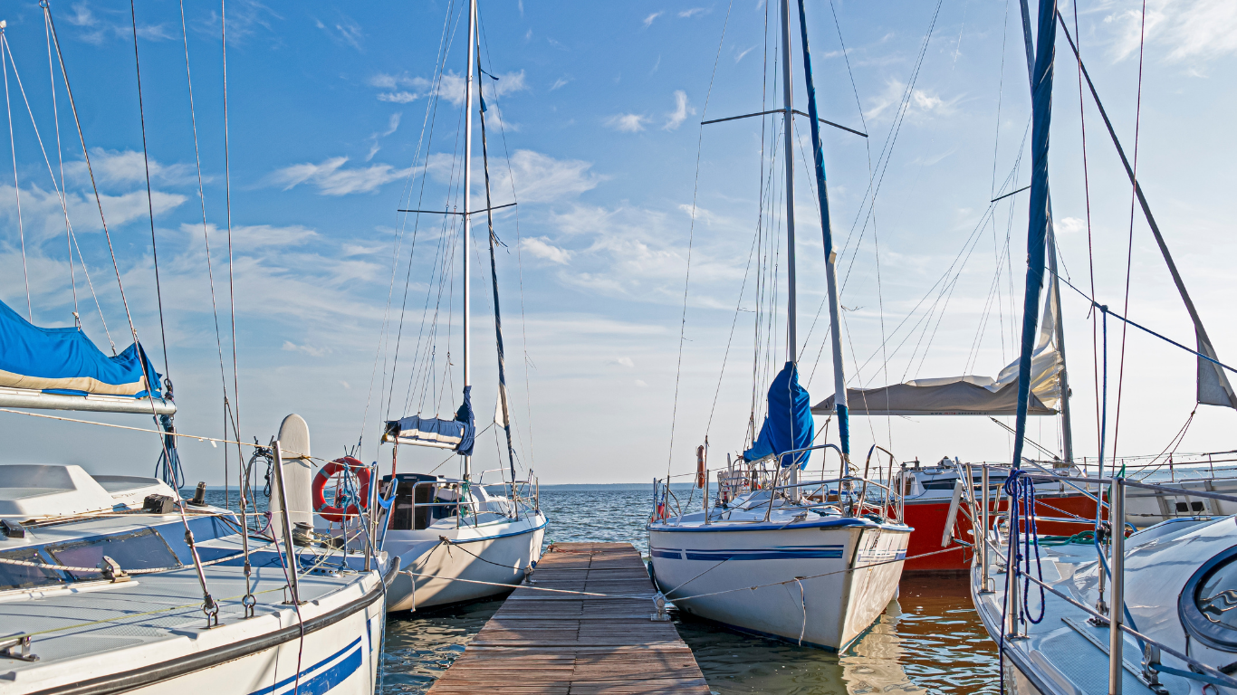 Sailboats docked at a pier on a sunny day, blue sky, calm water.