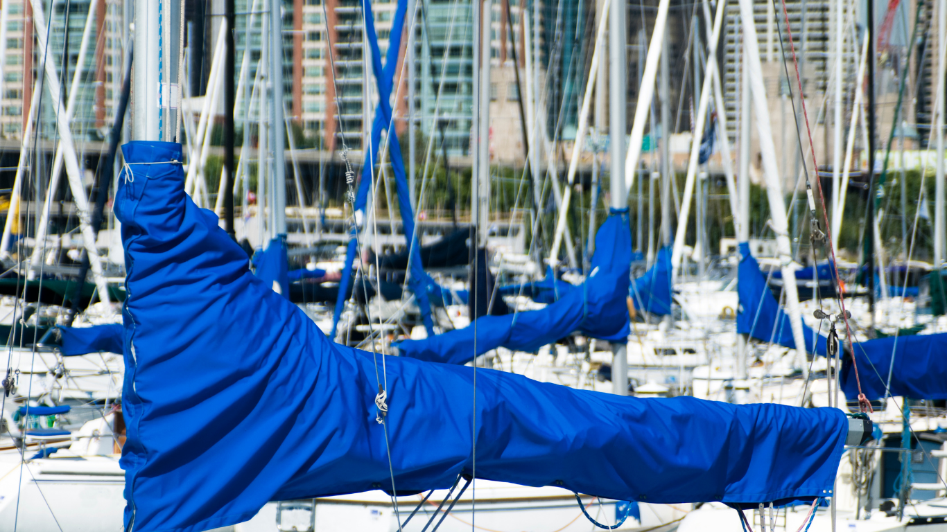 Blue sail folded on a sailboat mast in a marina with city buildings in the background.