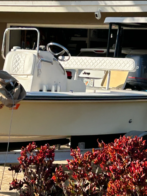 Tan and white boat on trailer, partially inside garage; red bush in foreground.
