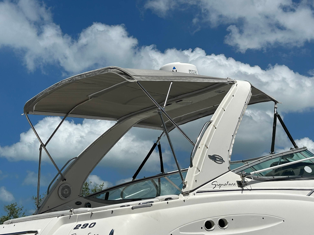 Boat with a grey canvas top and chrome supports against a blue sky.