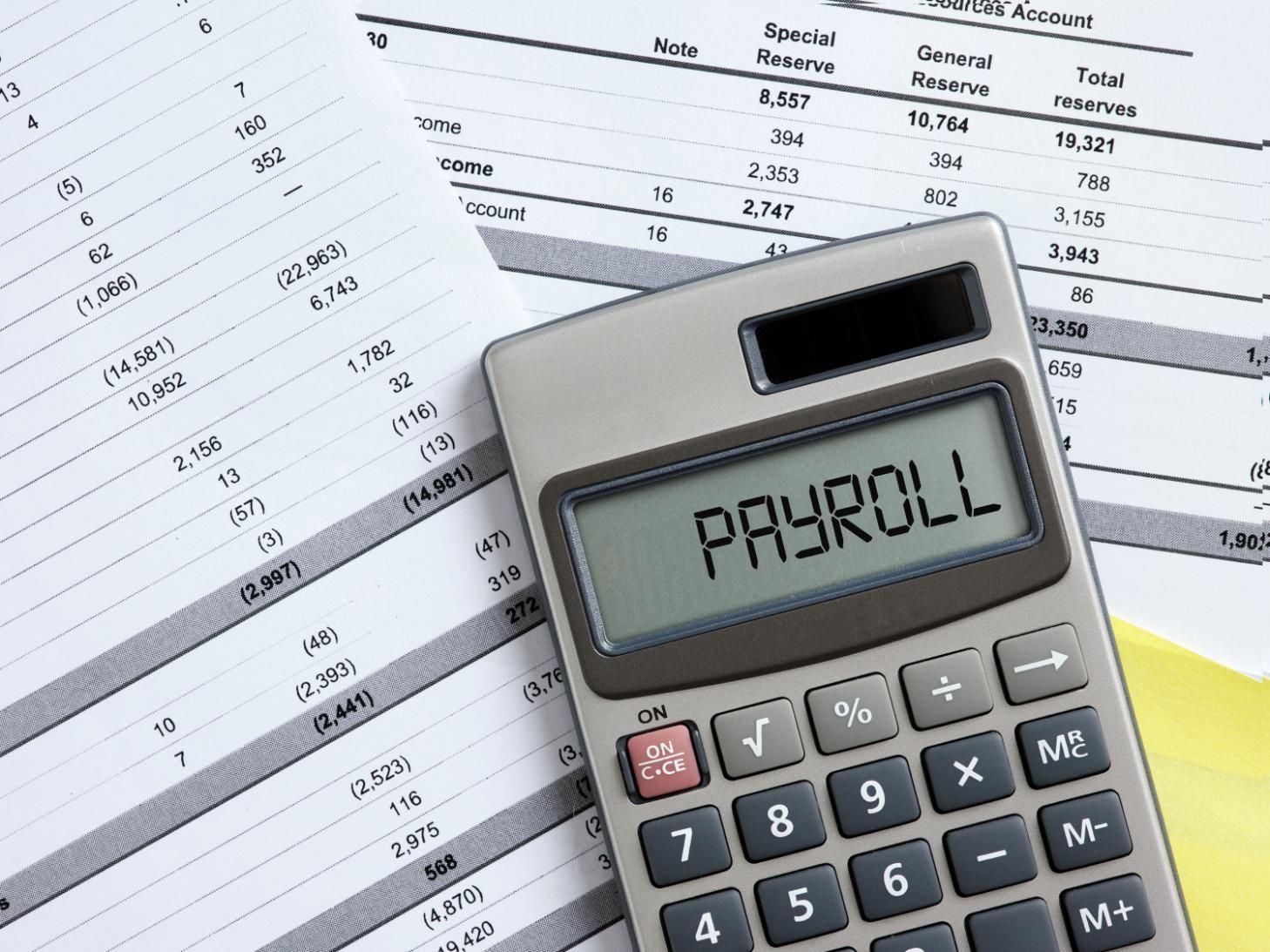 Calculator displaying "PAYROLL" on top of financial documents.