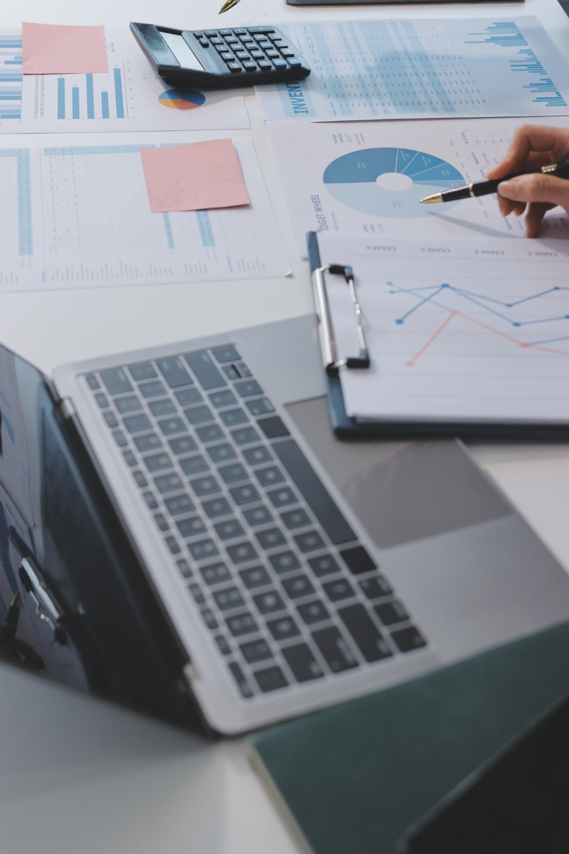 Laptop, documents, calculator, and hand pointing at chart, indicating data analysis.