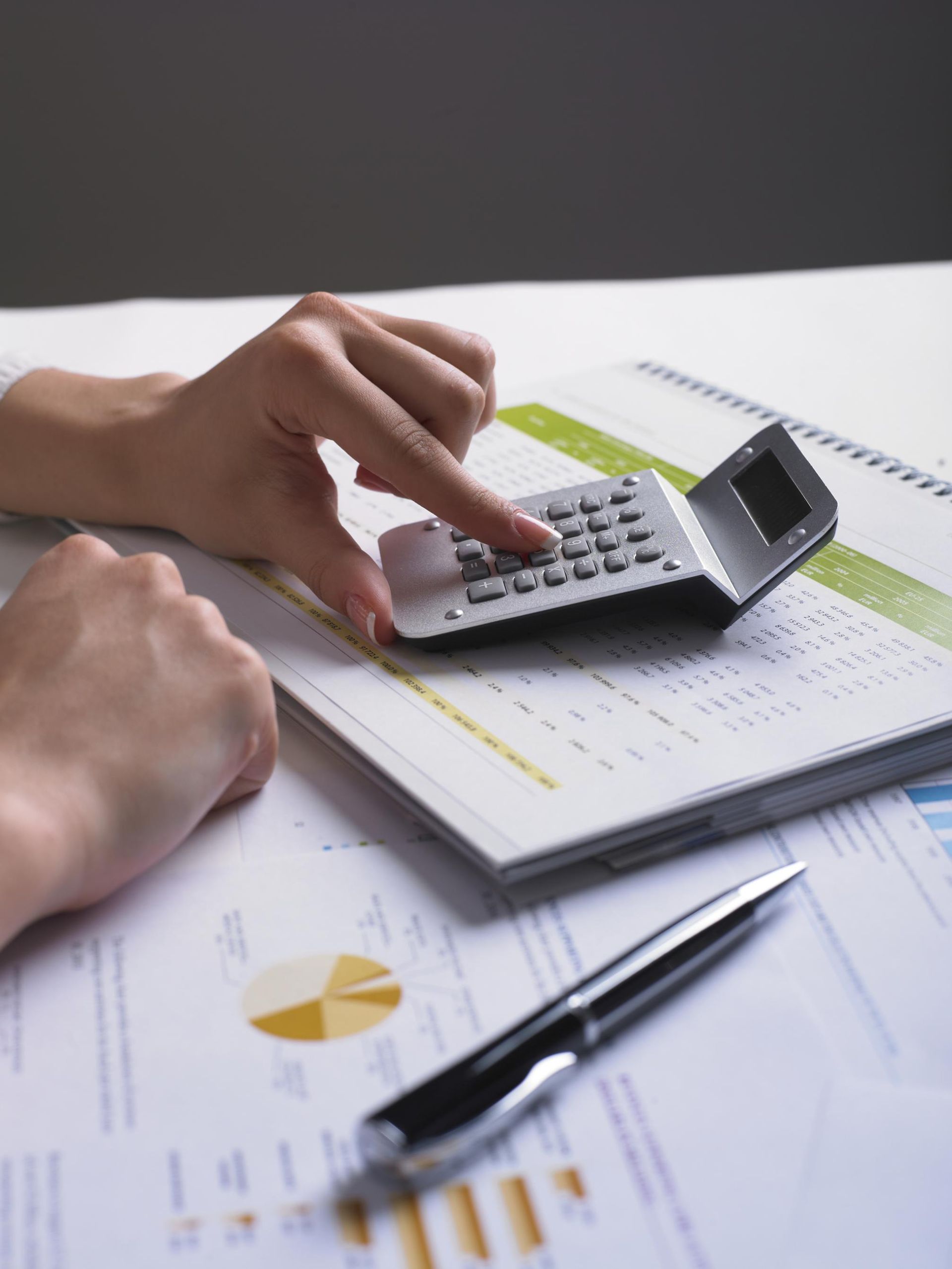 Hands using calculator on financial documents with a pen.