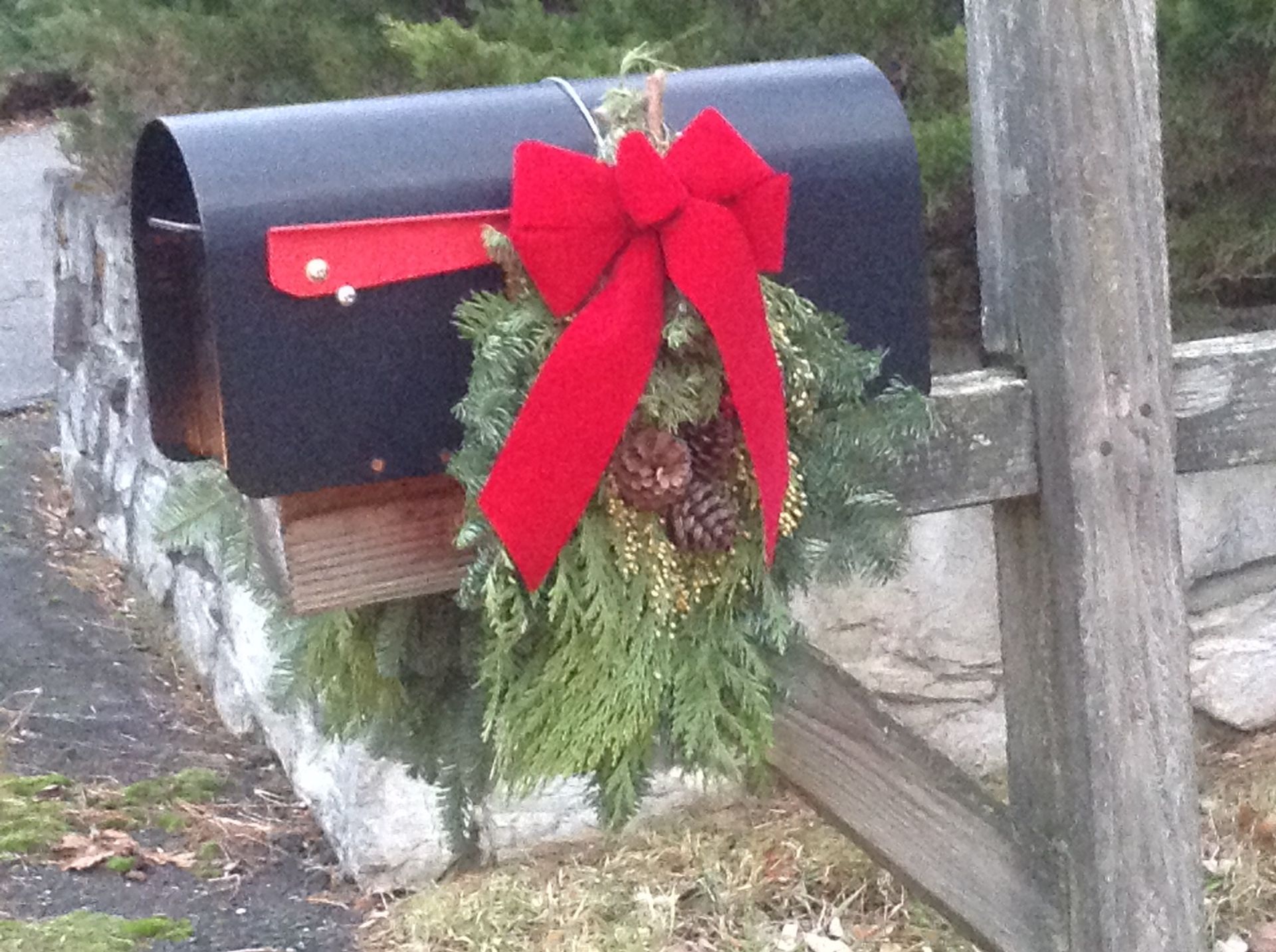 A black mailbox decorated for christmas with a red bow