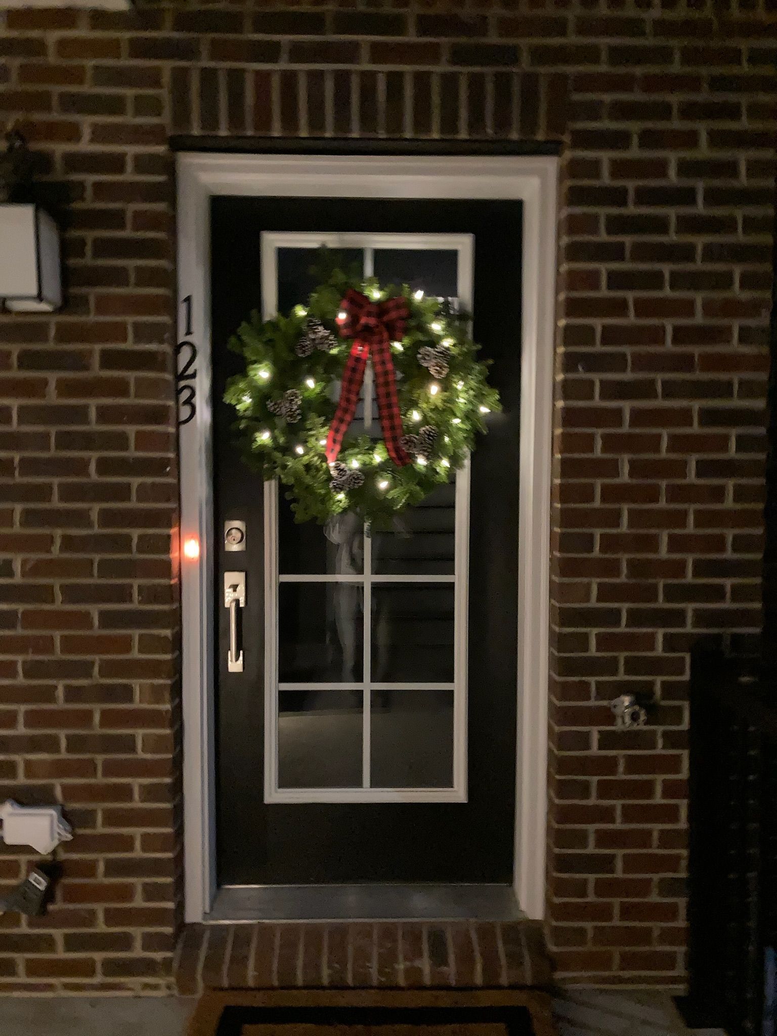 A christmas wreath is hanging on the front door of a brick house.