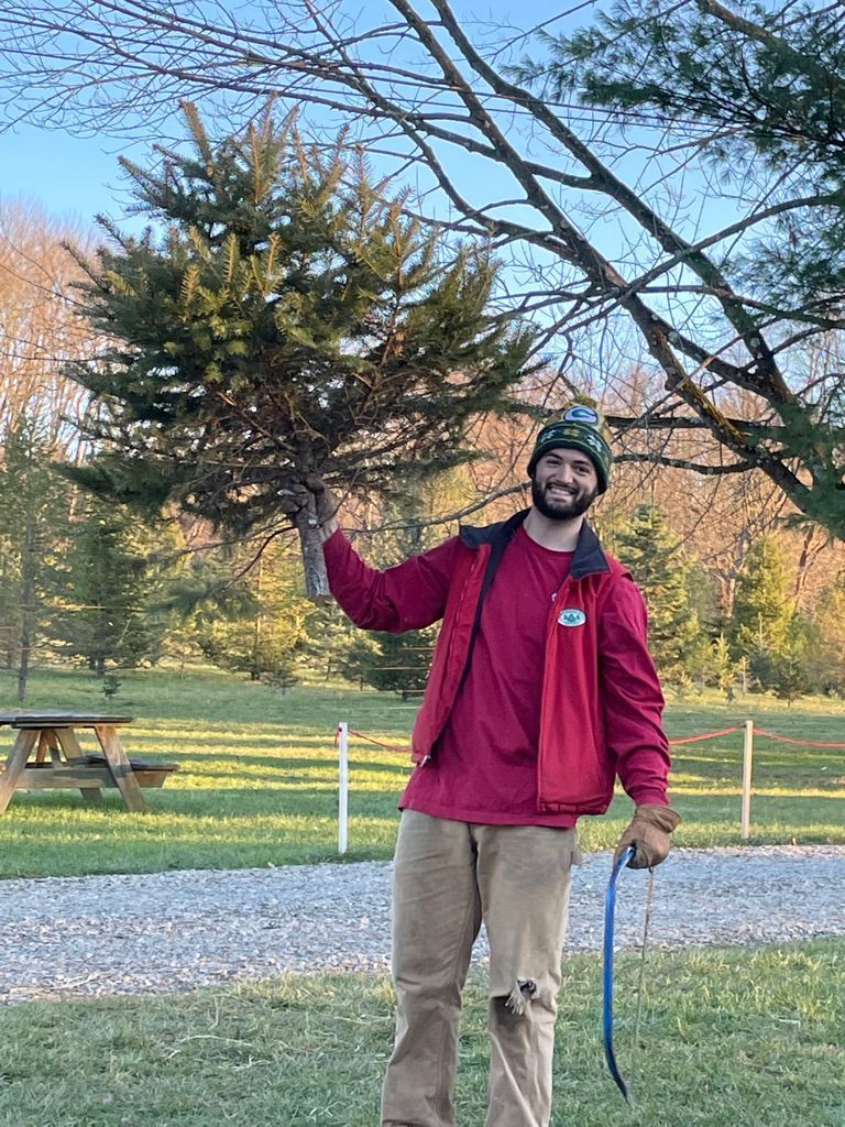 A man in a red jacket is standing in front of a tree holding a saw.