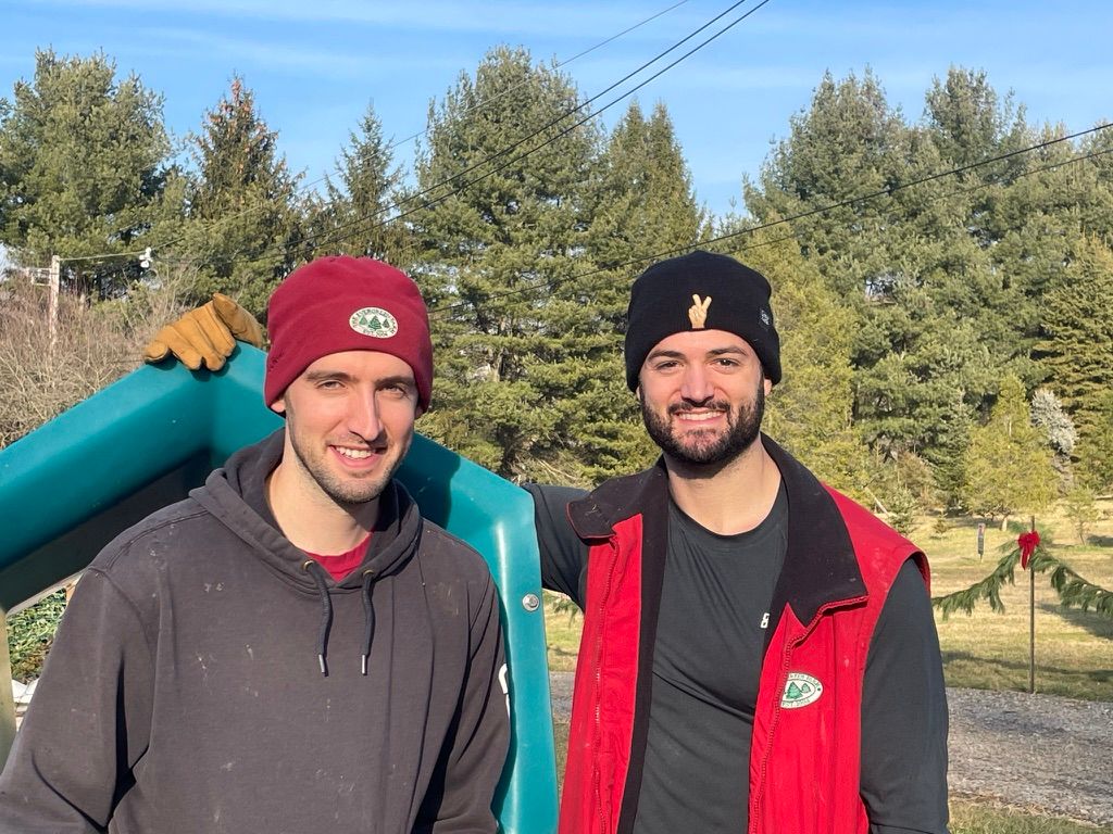 Two men are posing for a picture at a christmas tree farm.