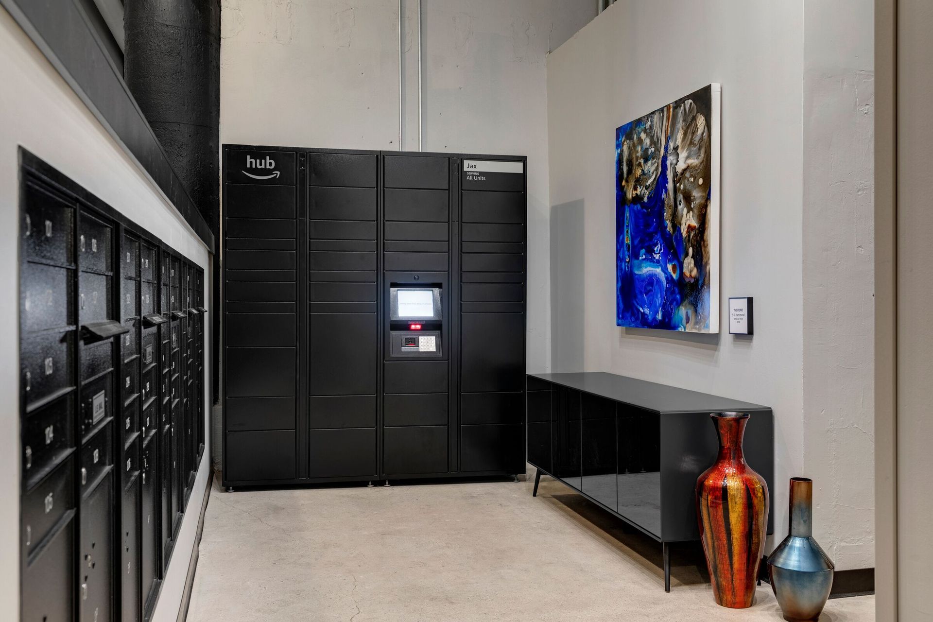 Interior mailroom with wall of small mail lockers and a large parcel locker system at The Jax in St. Paul, MN.