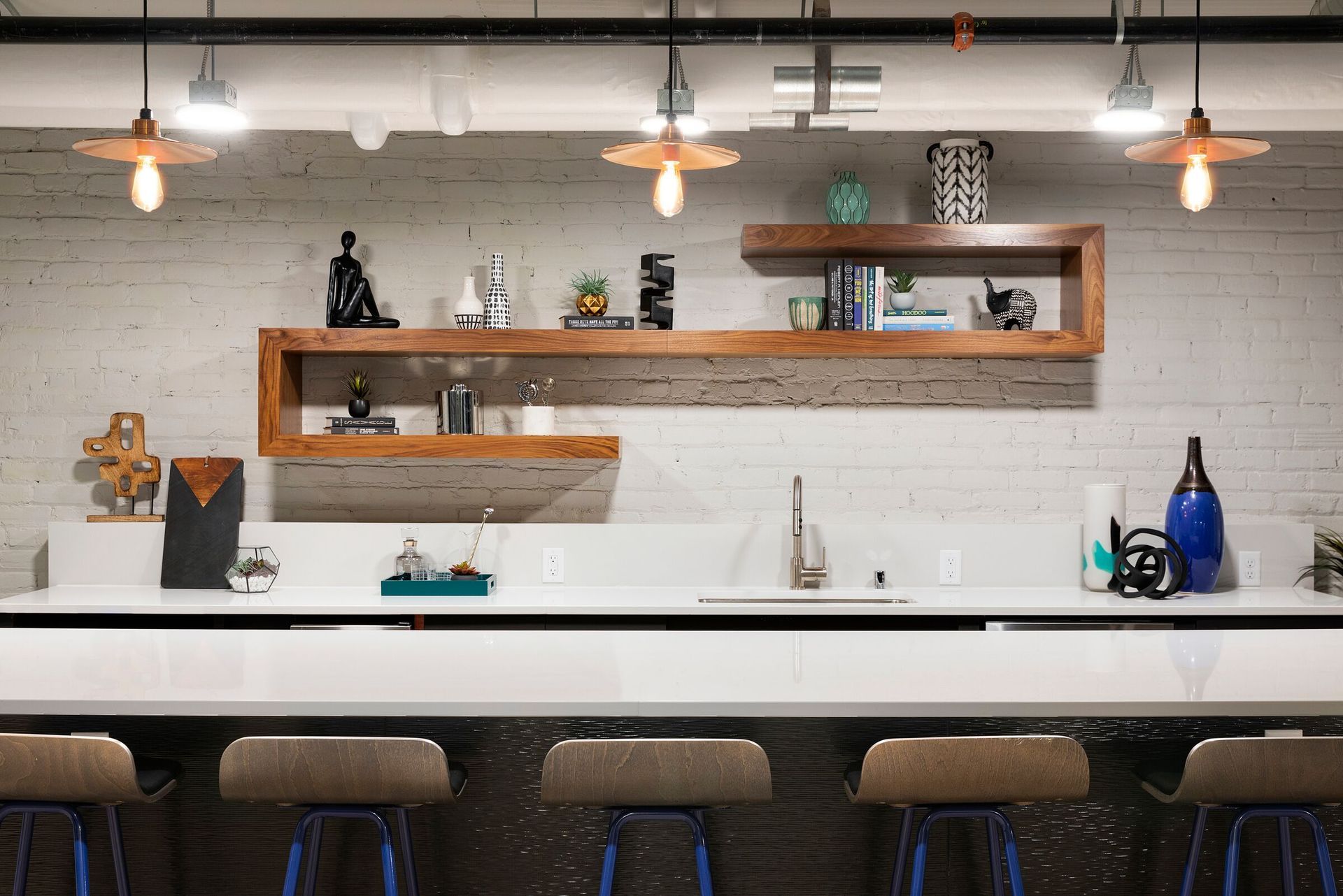 Modern community kitchen with white countertops, wooden shelves, and bar stools at The Jax in St. Paul, MN.