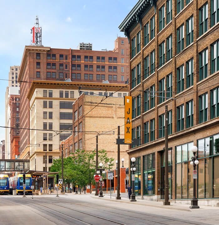 Street scene with brick buildings, trolley tracks, and a light rail train.