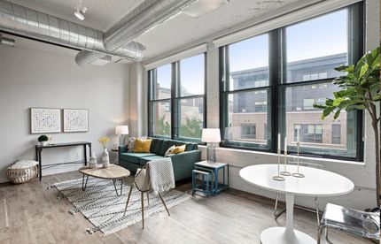 Living room with large windows, teal sofa, small coffee table, dining table.