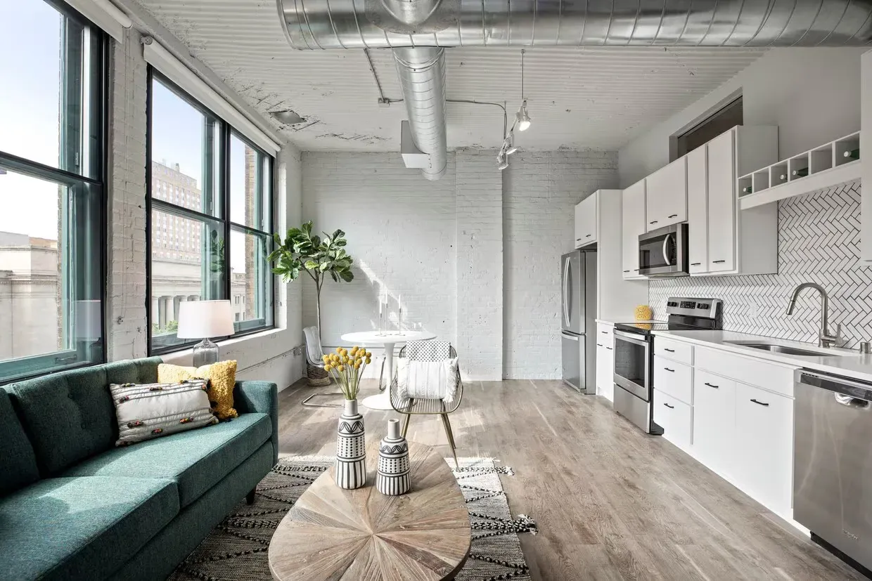 Open-concept living space with white kitchen, stainless appliances, green sofa, and large windows at The Jax in St. Paul, MN.