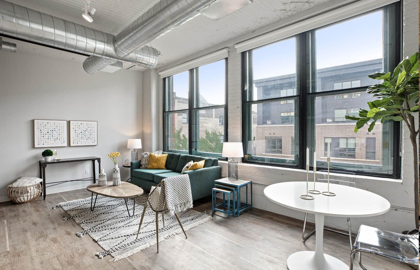 Modern living room with large windows, light wood floor, teal sofa, and round table.