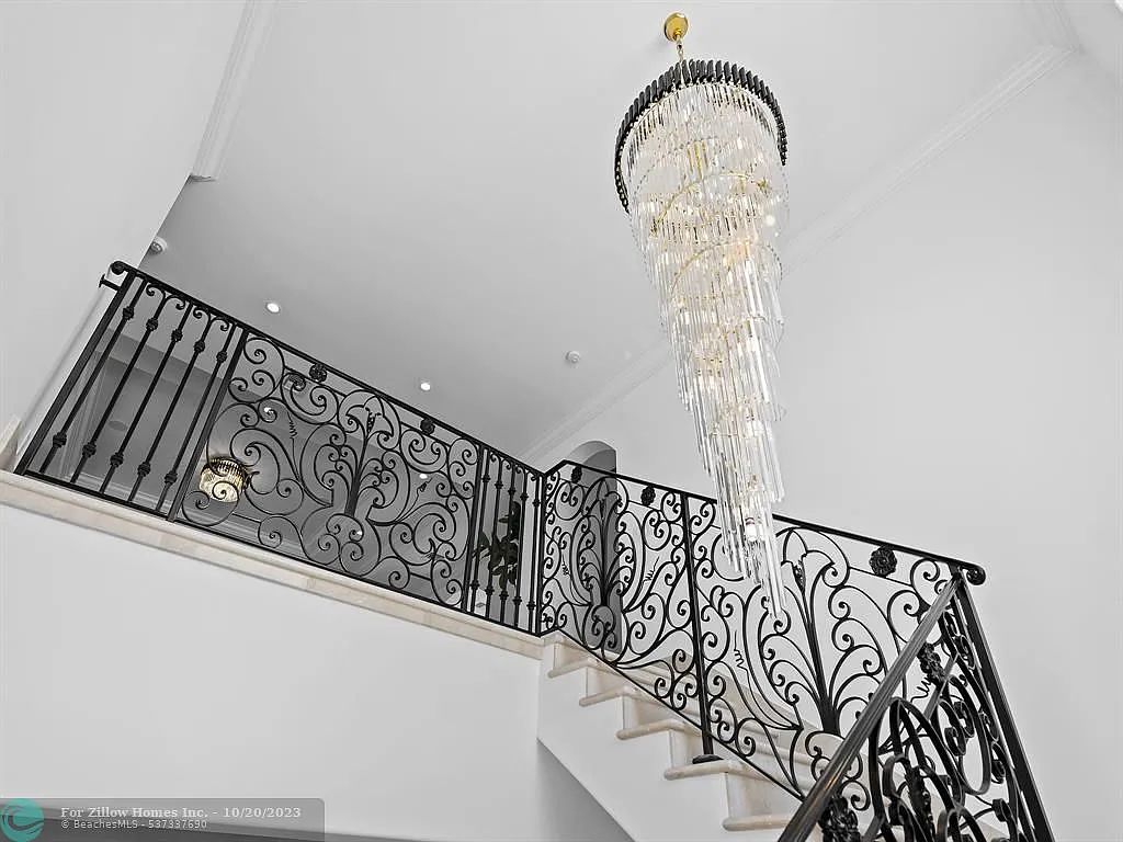 A staircase with a wrought iron railing and a chandelier hanging from the ceiling.